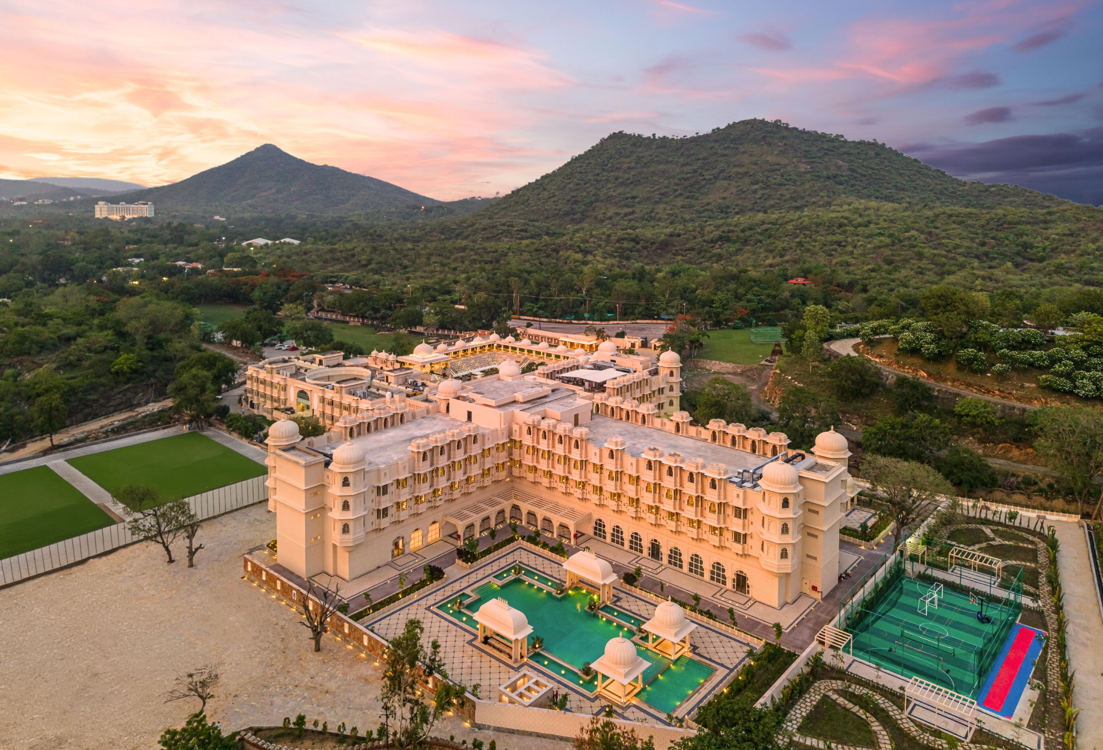 A large, multi-story building with a central courtyard, surrounded by lush greenery and hills.