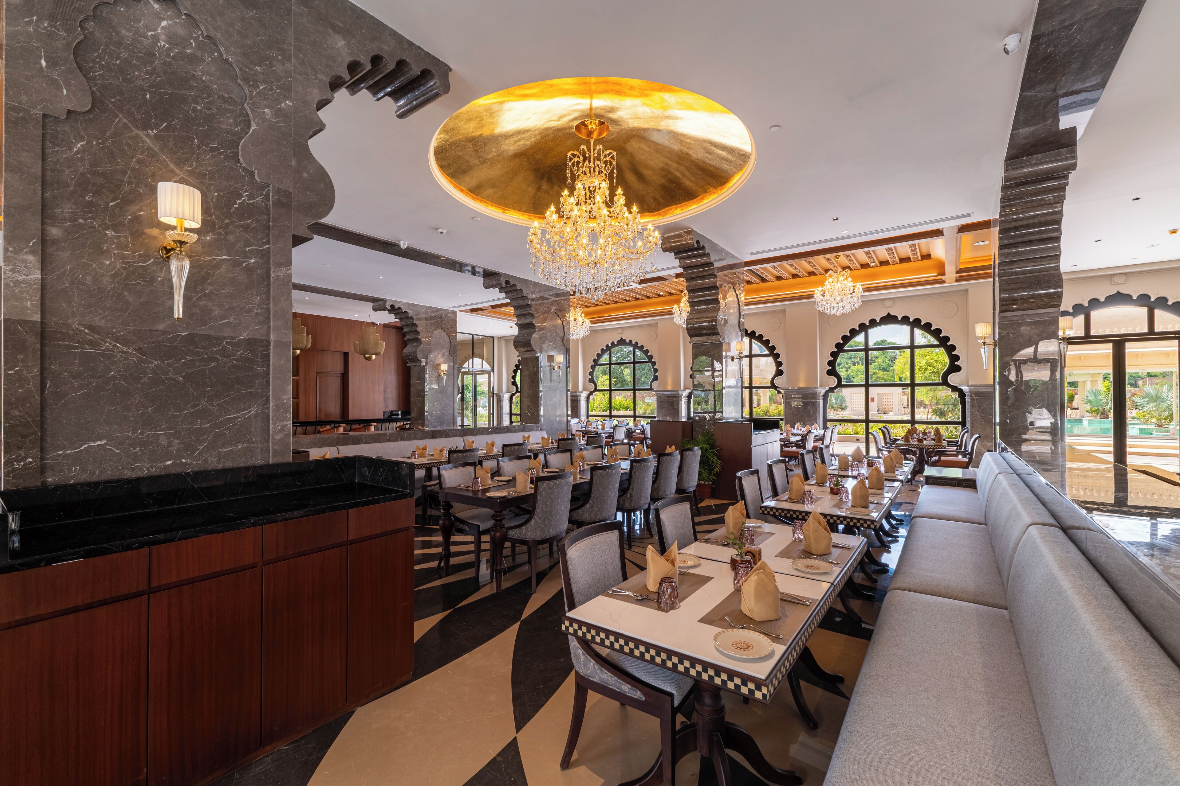 Un restaurante espacioso con techos altos, candelabros y una variedad de arreglos de asientos, incluyendo mesas y un largo banco.