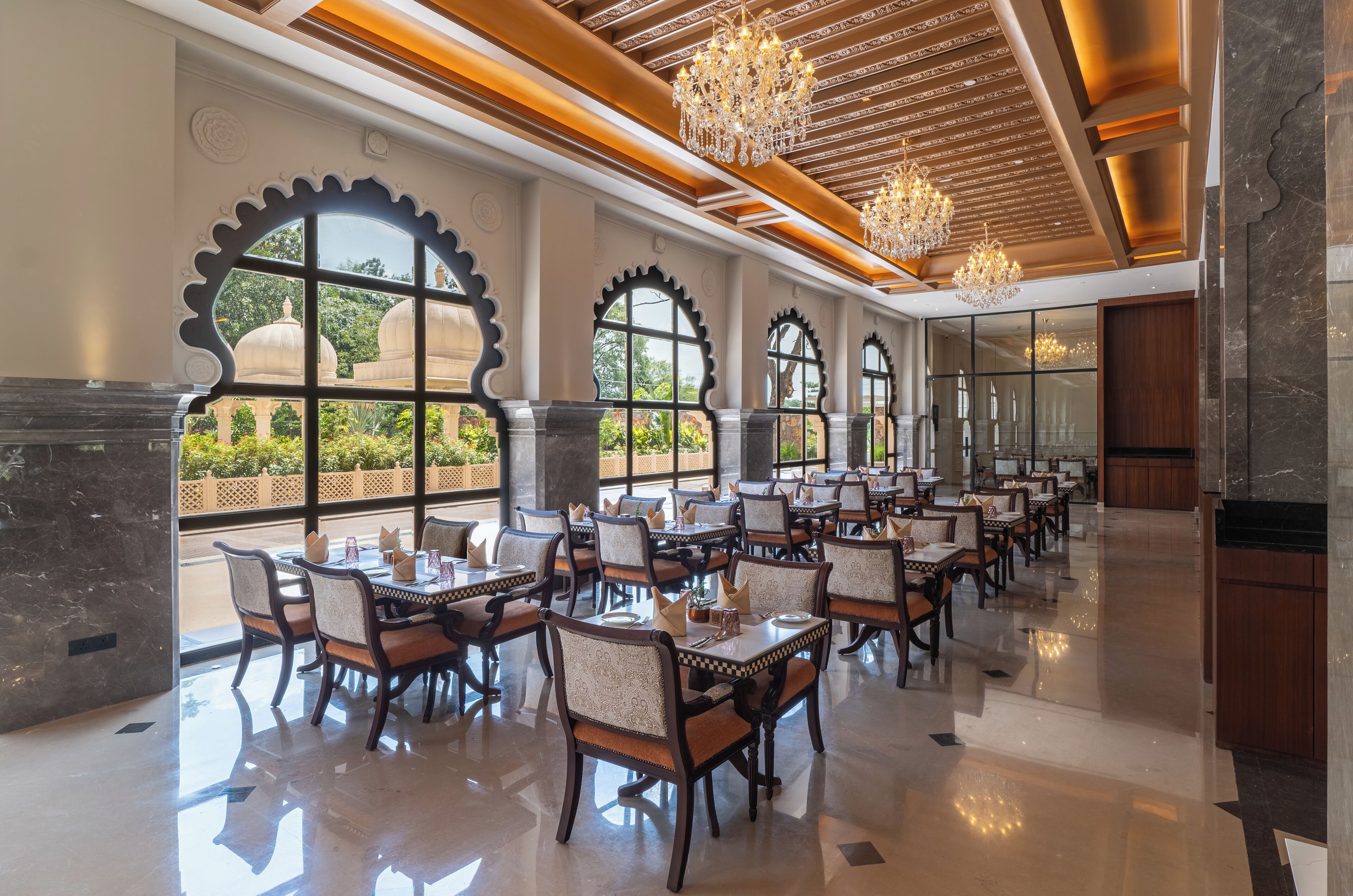 A spacious dining area with multiple tables and chairs, large arched windows, and chandeliers.