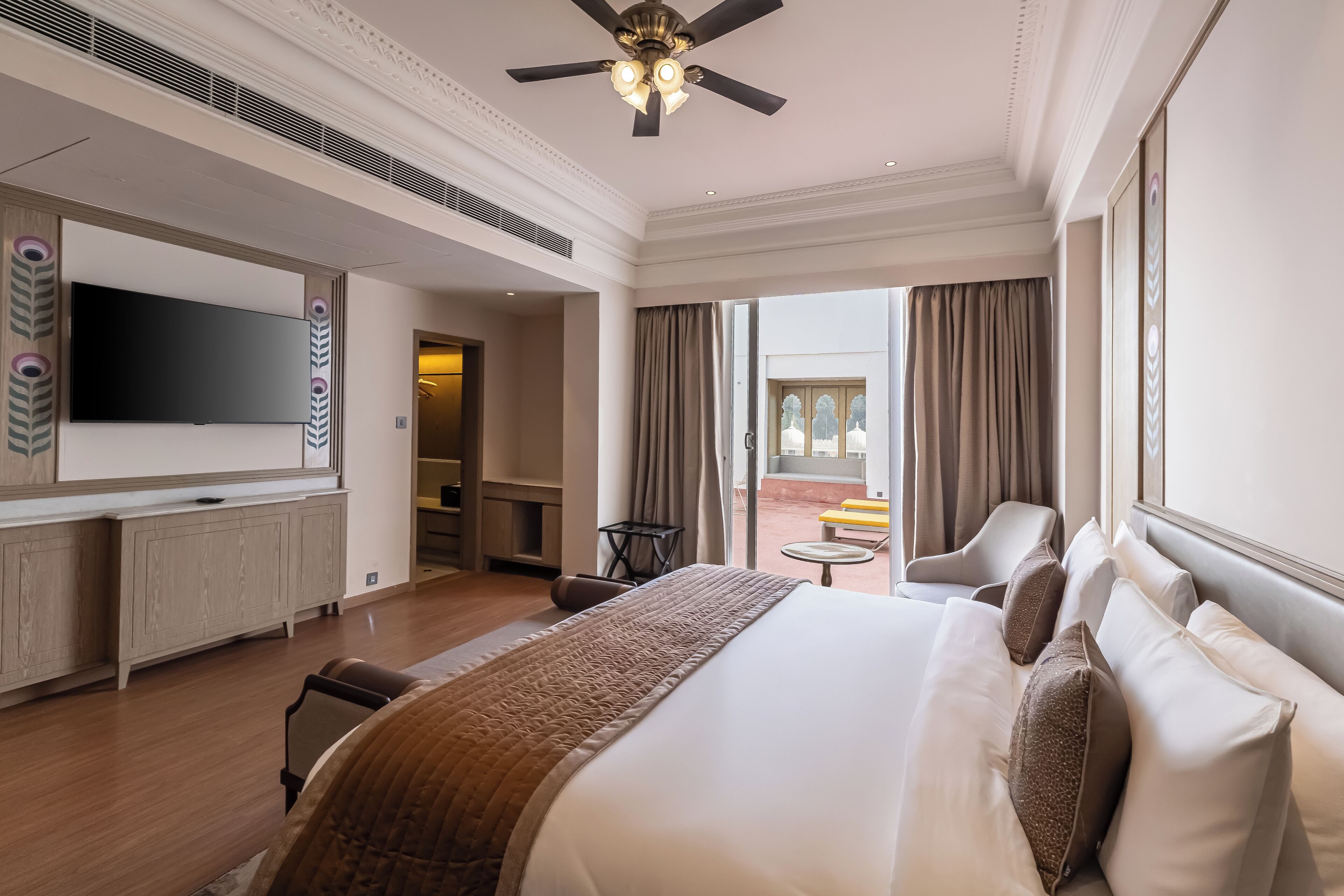 A hotel room with a large bed, a flat-screen TV, a ceiling fan, and a view of the outdoors.