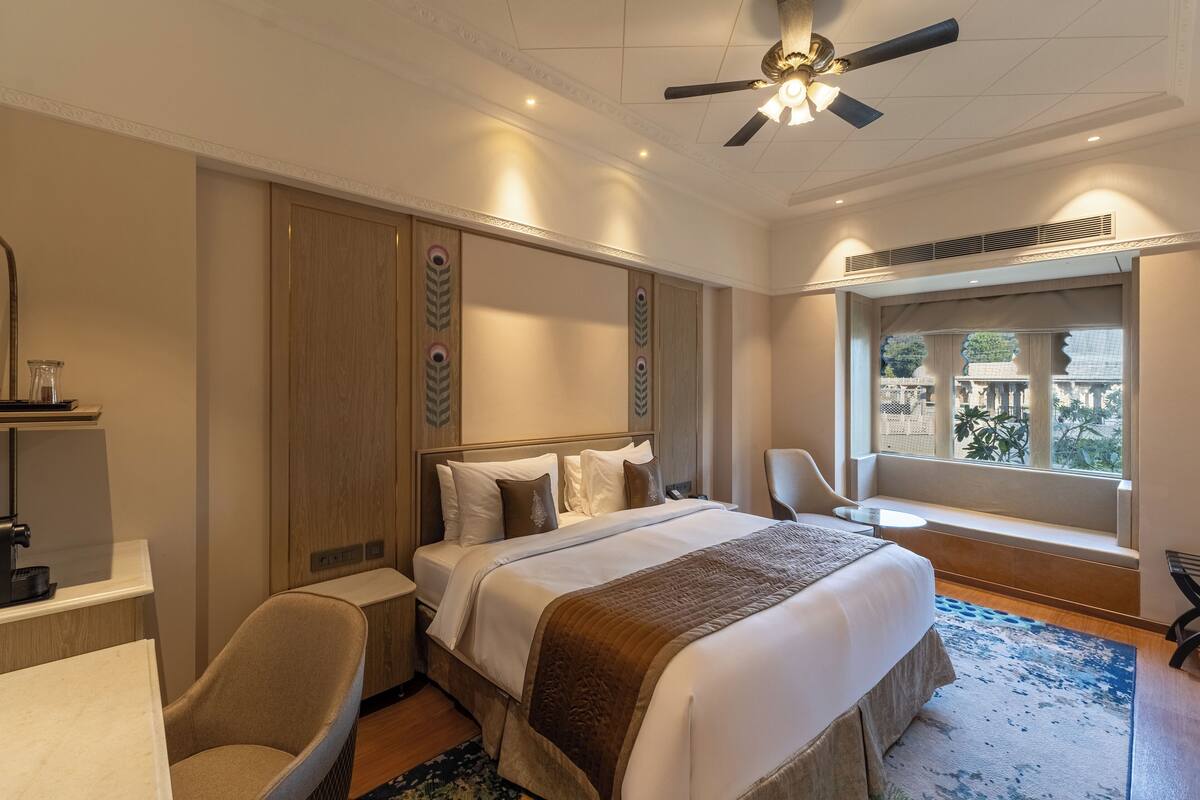 Ein Hotelzimmer mit einem großen Bett, einem Schreibtisch, einem Stuhl, einem Fenster mit Aussicht und einem Deckenventilator.
