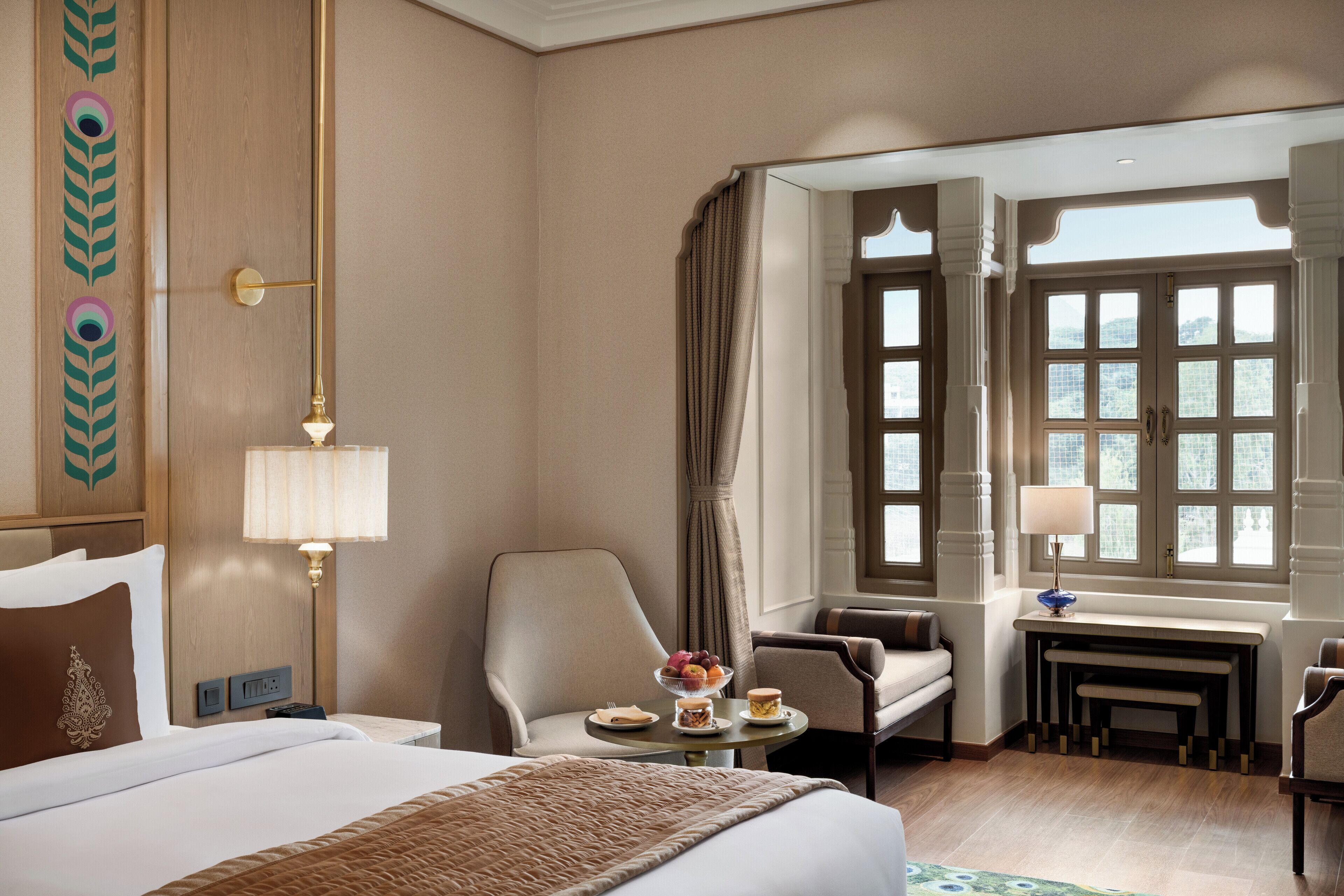 A hotel room with a large bed, a desk with a lamp, a chair, and a view of the outdoors through a window.
