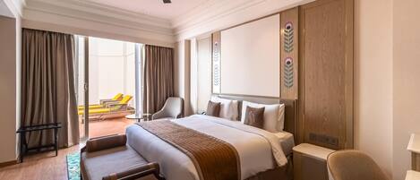 A hotel room with a large bed, a desk, a chair, a ceiling fan, and a view of the outside.