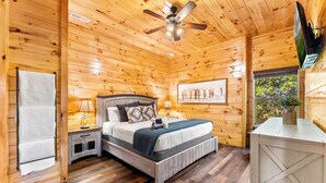 A wooden cabin bedroom with a bed, nightstands, a ceiling fan, and a window. - Family Cabin, Private Indoor Pool, Hot Tub, Views, Arcades, EV - 5 Min to Pkwy (Pigeon Forge)