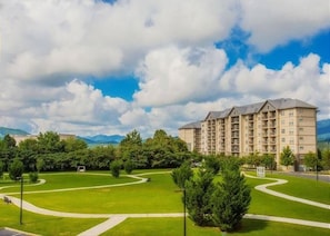 A multi-story hotel with a central courtyard, surrounded by greenery and a mountainous backdrop. - Mountain View Condo 1306 (Pigeon Forge)