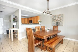 A dining area with a wooden table and chairs, a kitchen in the background, and a painting on the wall. - Mountain View Condo 1306 (Pigeon Forge)