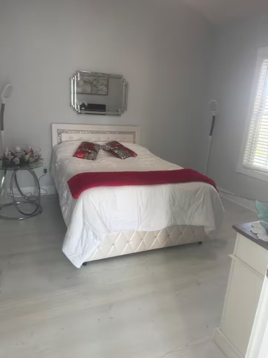 A bedroom with a bed, a bedside table, a mirror, and a window.