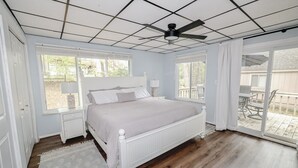 Une chambre avec un grand lit, une table de chevet, un ventilateur de plafond et une vue sur le jardin à travers une porte-fenêtre coulissante.
