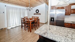 Une cuisine moderne avec des meubles en bois, un réfrigérateur en acier inoxydable, des comptoirs en granit et un coin repas avec des chaises et une table en bois.