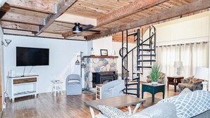 Un vaste salon doté d’une cheminée en pierre, d’un plafond en bois et d’un escalier.