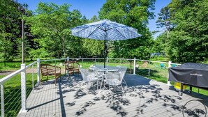 An outdoor deck with a table and chairs, a patterned umbrella, and a grill. - Firepit, Deck & Views | Stairs to Lake Michigan (Montague)