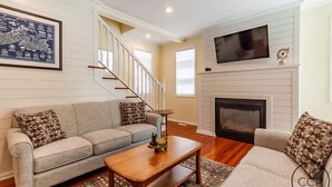 A living room with a sofa, coffee table, fireplace, and a framed map on the wall. - Firepit, Deck & Views | Stairs to Lake Michigan (Montague)