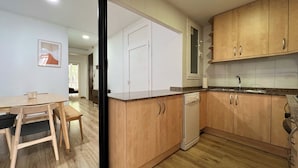 Een moderne keuken met houten kastjes, een vaatwasser en een eethoek met een tafel en stoelen.