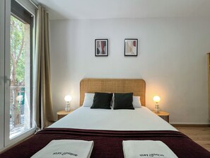Une chambre d’hôtel avec un grand lit, deux tables de chevet avec des lampes, une fenêtre avec des rideaux et deux tableaux encadrés accrochés au mur.
