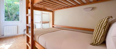 A bunk bed with a wooden frame and a white mattress. There is a window with a view of trees outside.