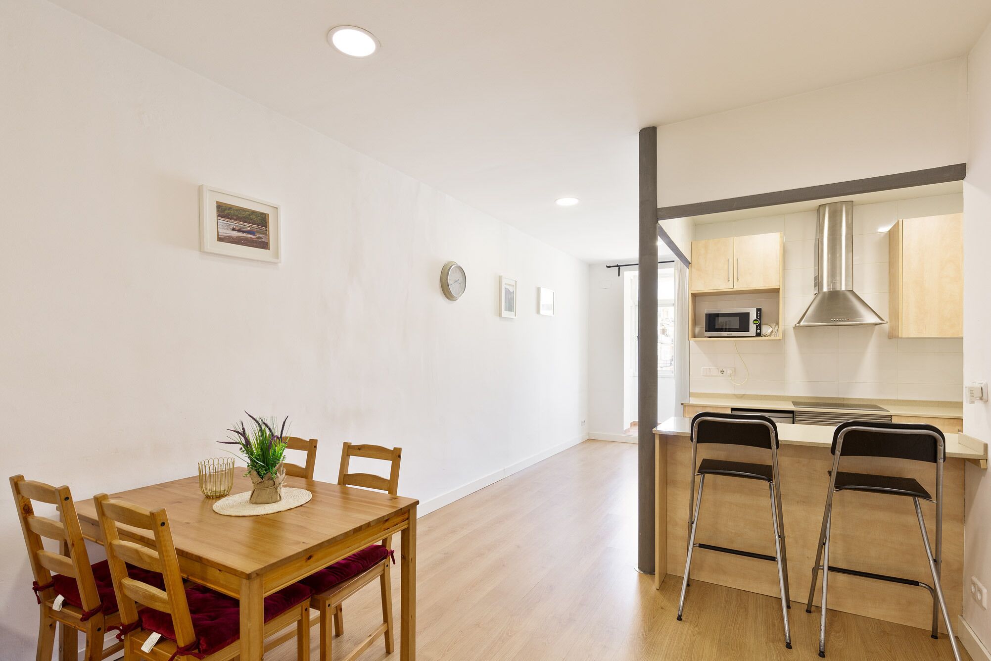 A modern kitchen with a microwave, stove, and stainless steel range hood. There is a dining area with a wooden table and chairs, and a small potted plant on the table.