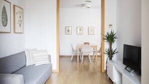 A modern living room with a grey sofa, a dining table with chairs, a TV on a white stand, and framed botanical prints on the wall. - Stay U-nique Apartments Villarroel (Barcelona)