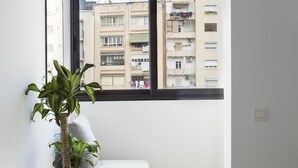 A modern bedroom with a large window, a grey sofa, a potted plant, and a bed. - Stay U-nique Apartments Villarroel (Barcelona)