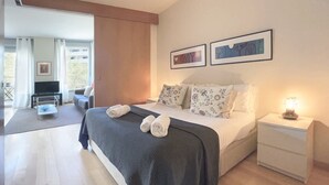 A modern bedroom with a large bed, a bedside table with a lamp, and a TV in the corner.