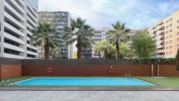 A swimming pool with two lifebuoys, surrounded by palm trees and modern buildings.