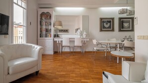 A spacious living area with a white sofa, a dining table with chairs, a kitchen area with a white cabinet, and a bookshelf. - Stay U-nique Apartment Creu Coberta II (Barcelona)