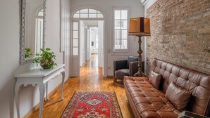 A hallway with a brown leather sofa, a white console table with a plant, a large mirror, and a brick wall. - Stay U-nique Apartment Creu Coberta II (Barcelona)