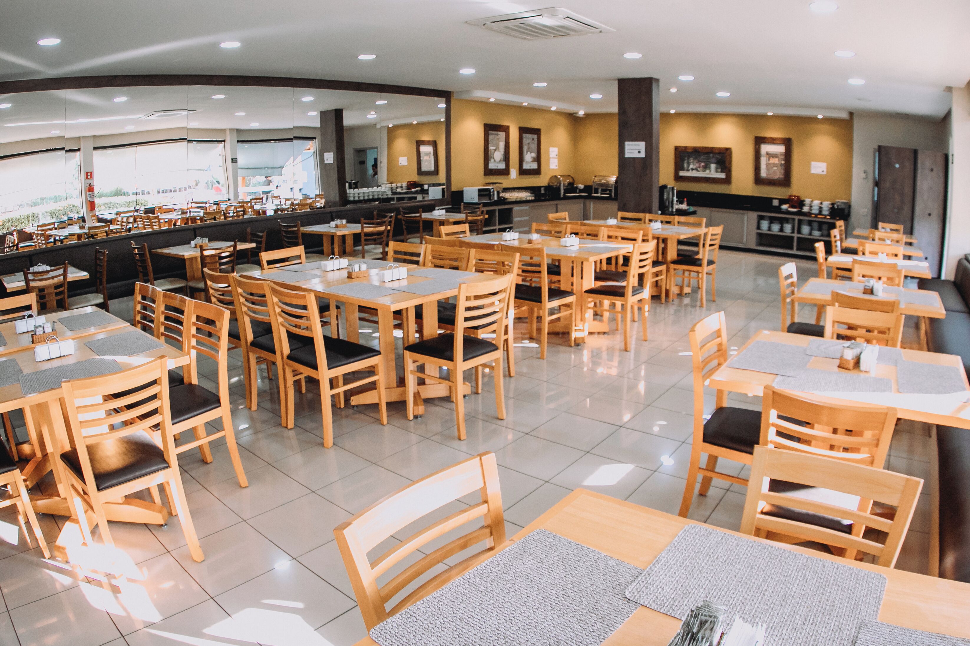 A spacious restaurant with multiple wooden tables and chairs, a counter with a beverage station, and framed artwork on the walls.