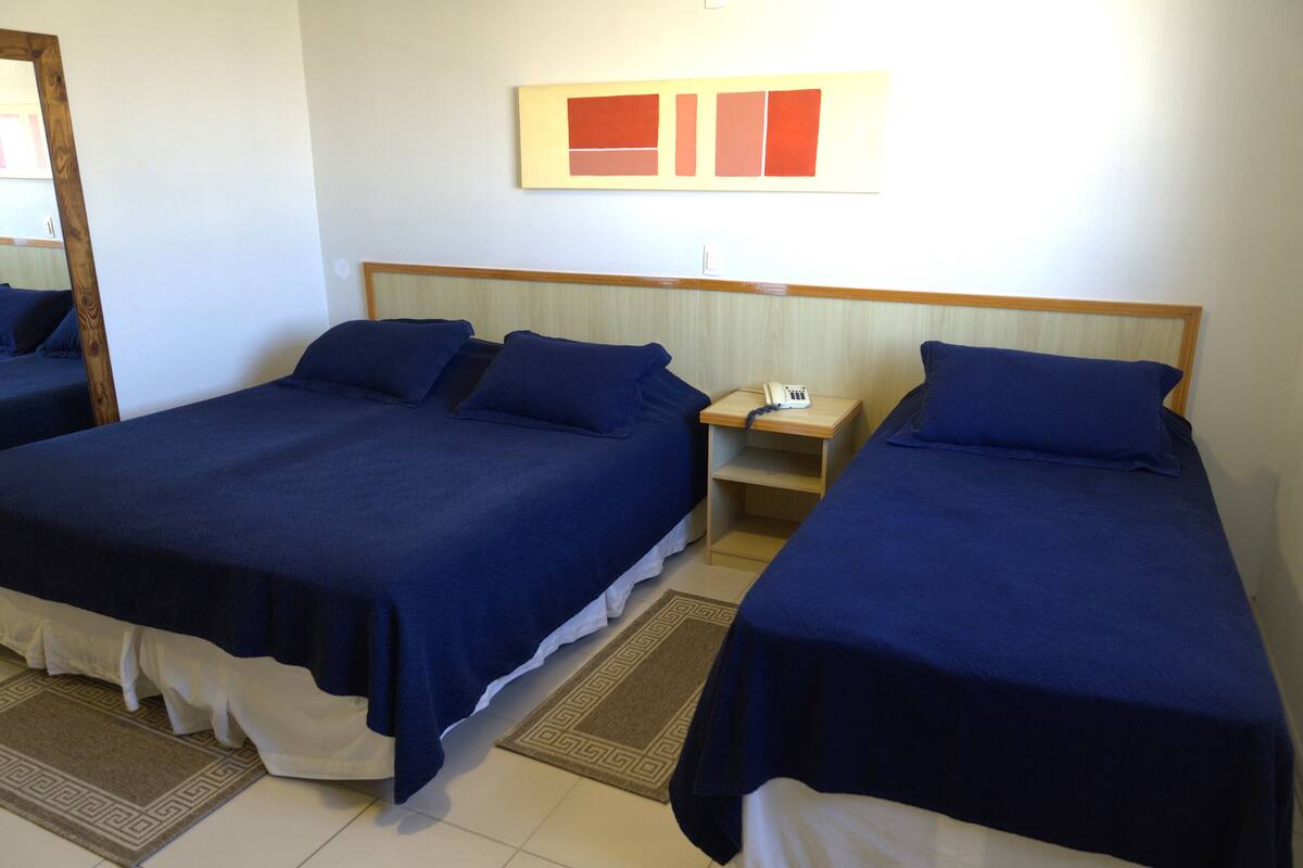 A hotel room with two beds, a nightstand, a mirror, and a wall art piece.
