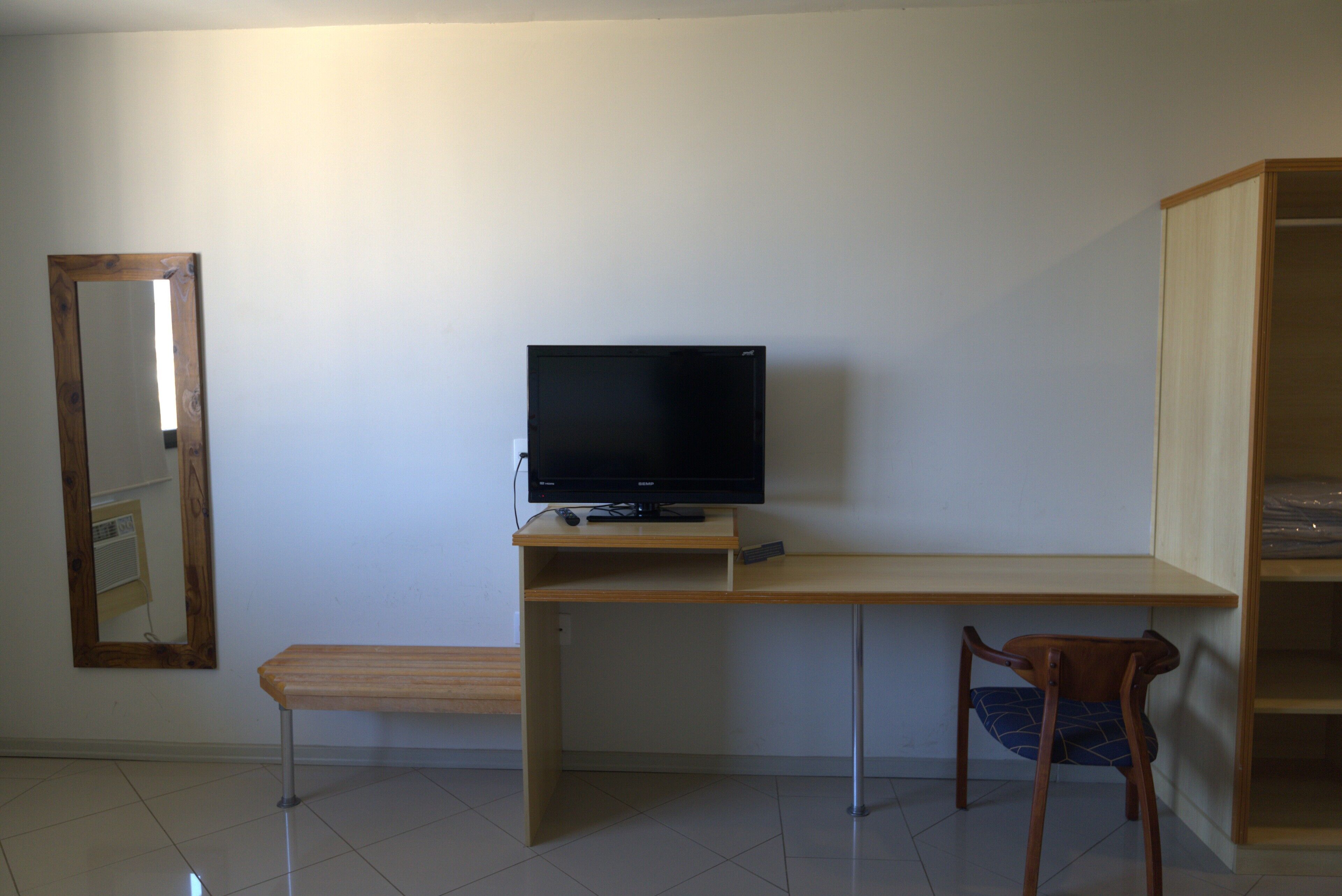 Ein Zimmer mit Schreibtisch aus Holz, Fernseher, Stuhl und Spiegel an der Wand.