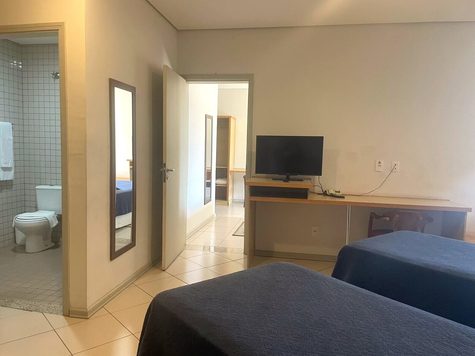 Habitación de hotel con cama, televisión, escritorio y baño visible a través de una puerta abierta.