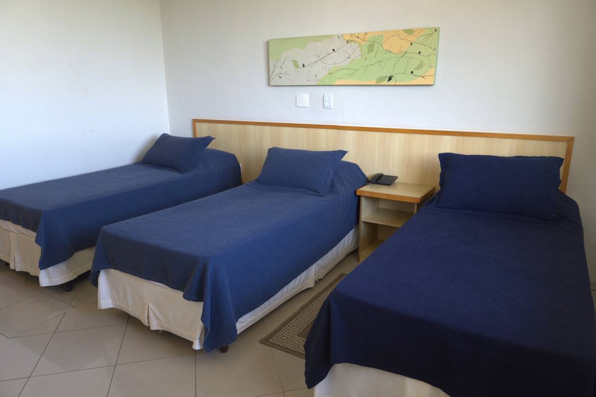 A hotel room with three single beds, a wooden headboard, a bedside table with a phone, and a map on the wall.