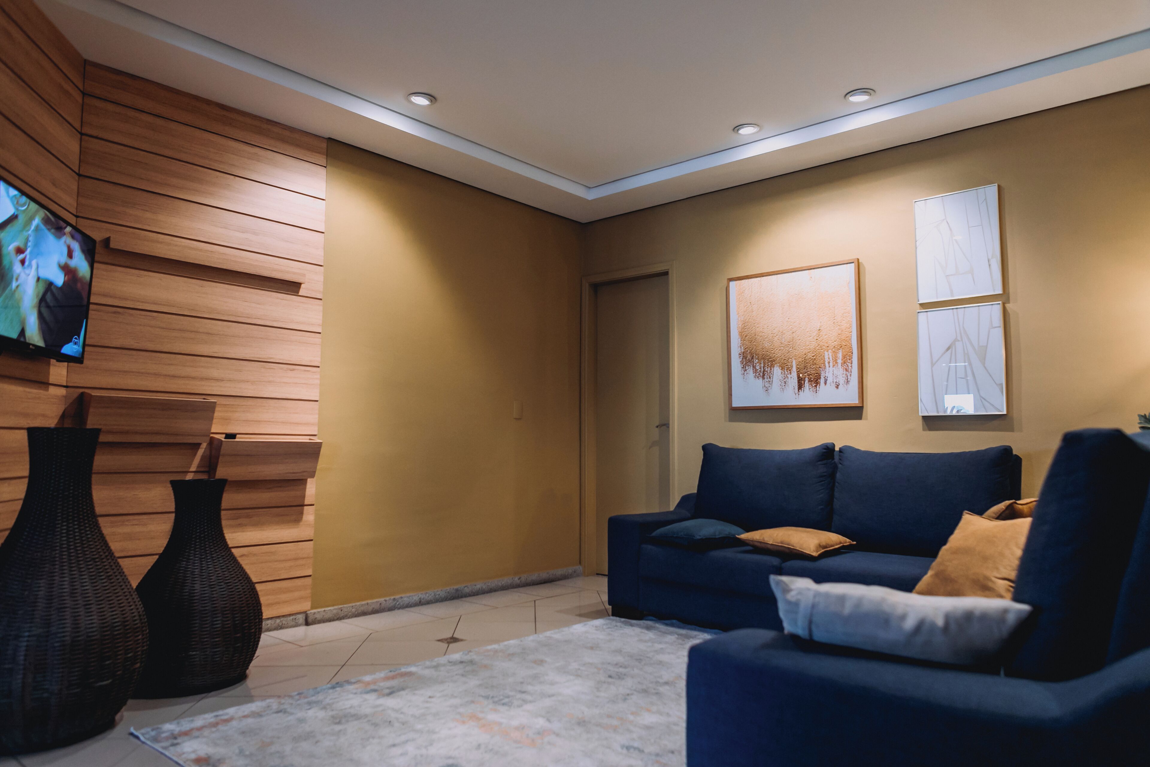 Ein modernes Wohnzimmer mit einem blauen Sofa, zwei großen Vasen und einem Flachbildfernseher an einer Holzwand.