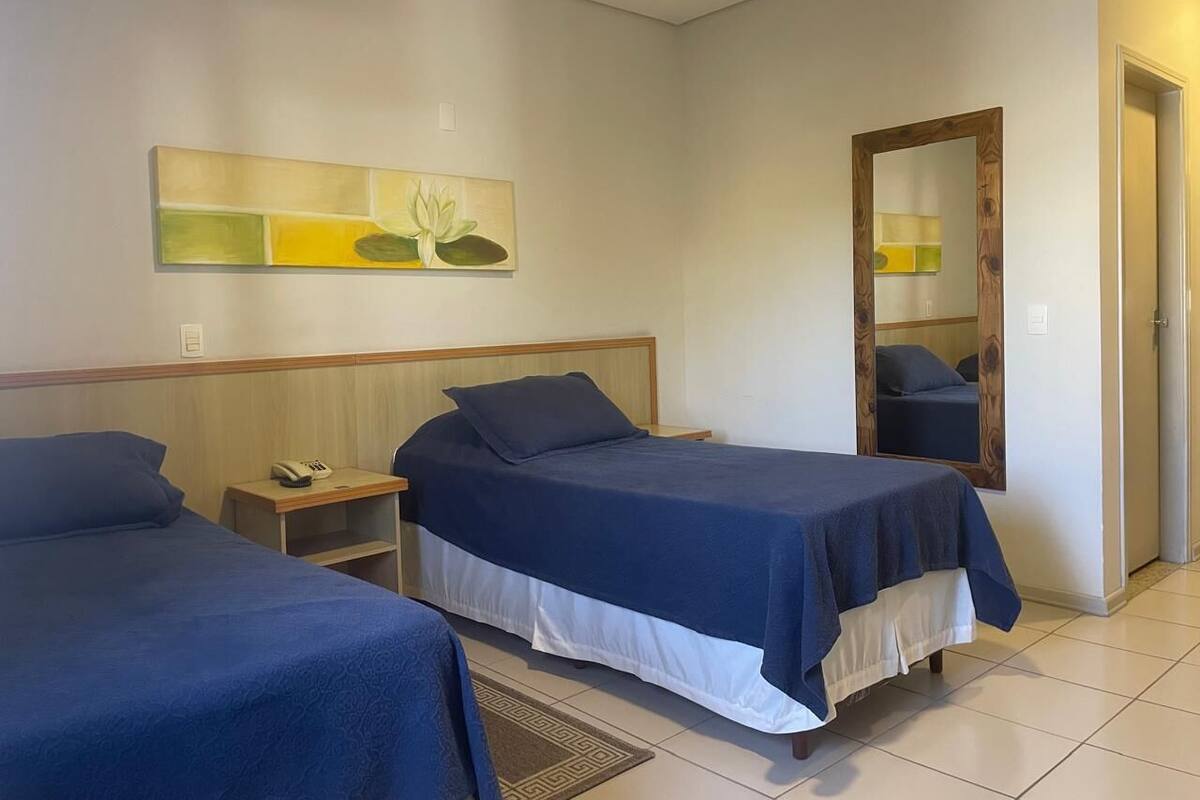 A hotel room with two beds, a nightstand with a telephone, a mirror, and a wall art piece.