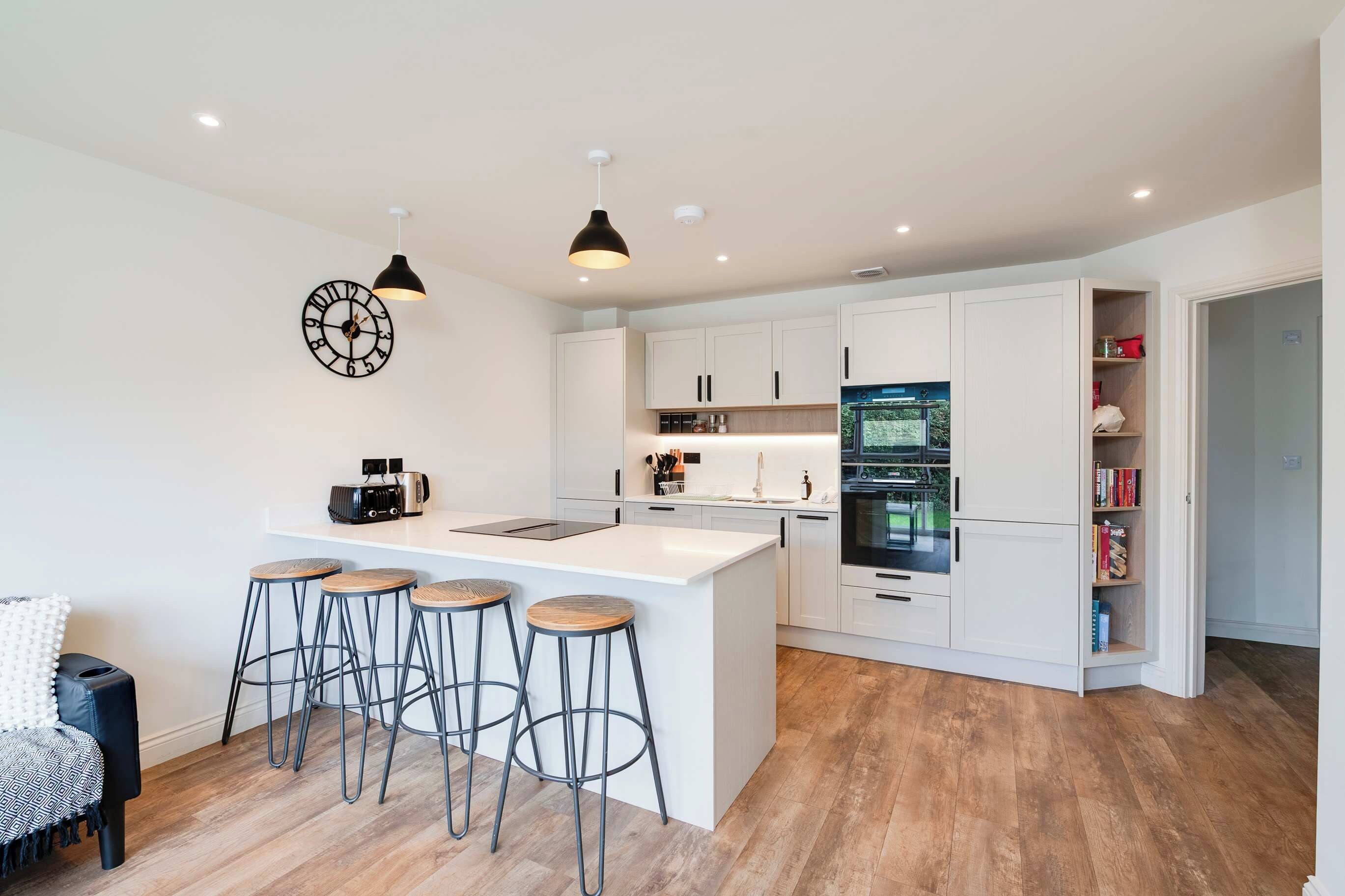 A modern kitchen with a central island, bar stools, white cabinetry, and a built-in oven.