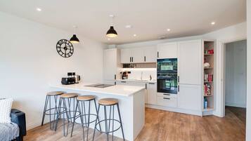 A modern kitchen with a central island, bar stools, white cabinetry, and a built-in oven.