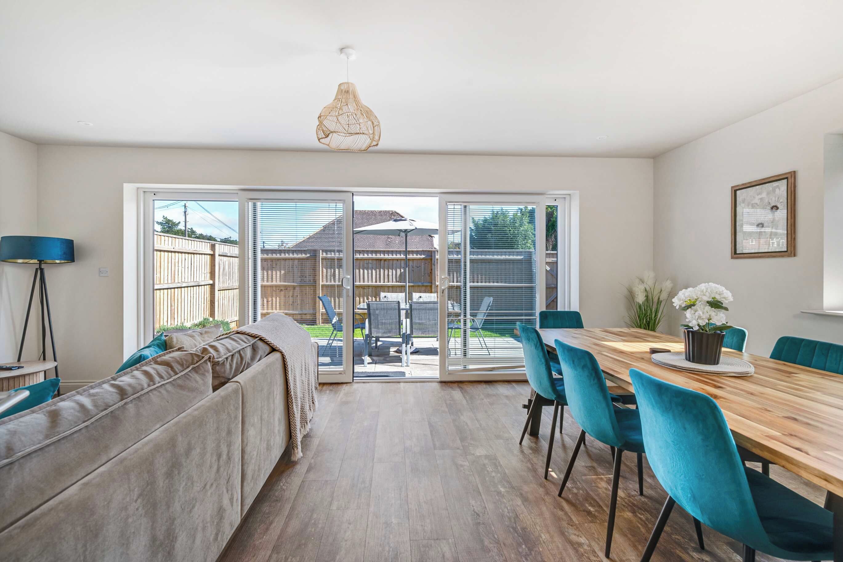 Een moderne keuken met een eethoek, met een houten tafel, blauwgroene stoelen en een groot raam met uitzicht op de achtertuin.