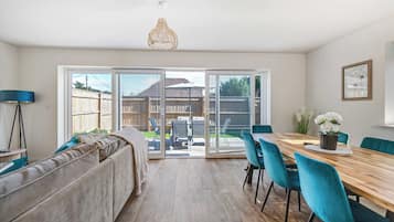 Eine moderne Küche mit Essbereich, ausgestattet mit einem Holztisch, smaragdgrünen Stühlen und einem großen Fenster mit Blick auf den Garten.