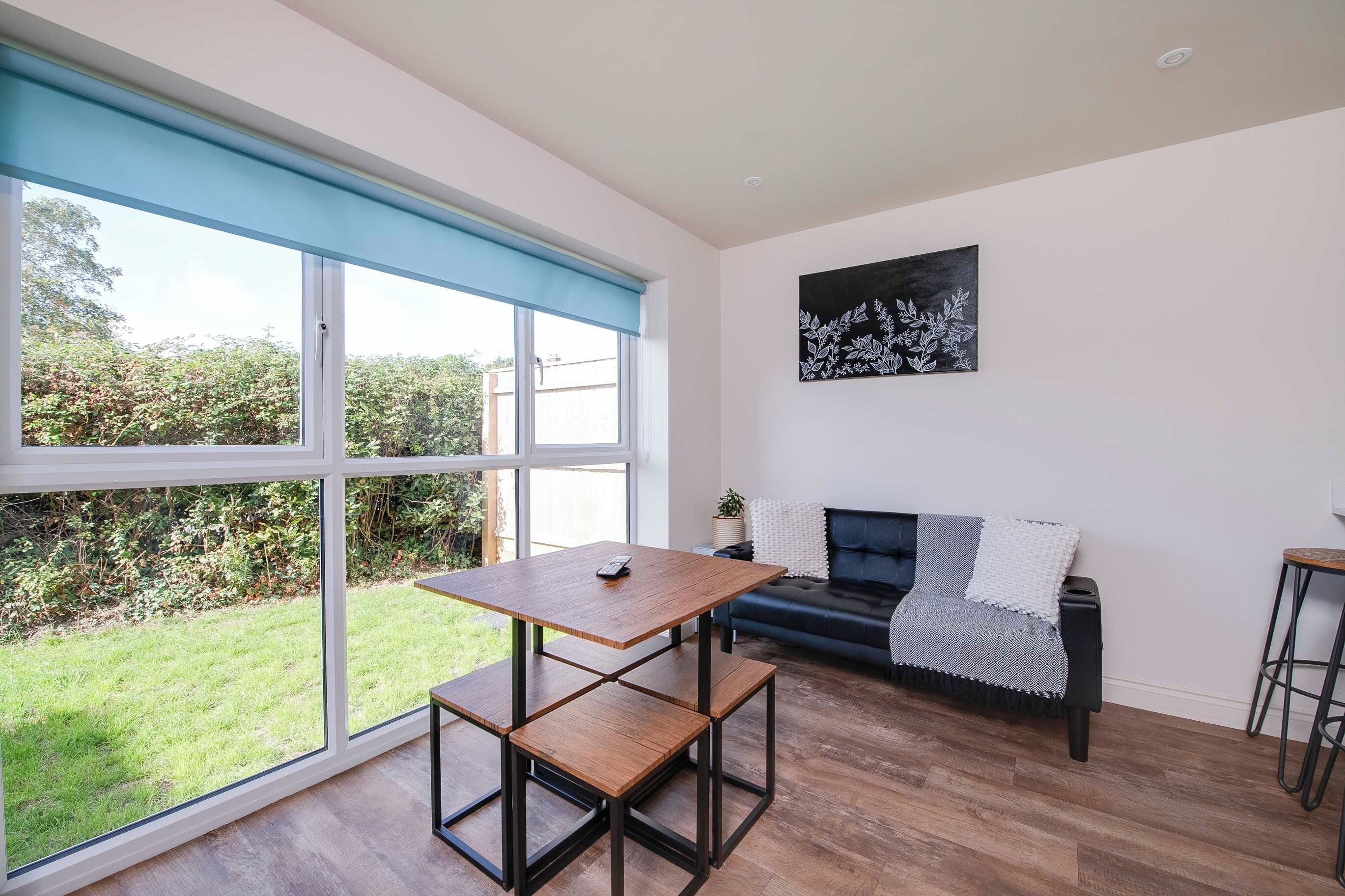 A modern living room with a large window, a black leather sofa, a wooden coffee table, and a minimalist artwork on the wall.