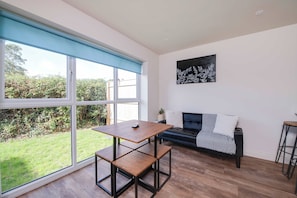A modern living room with a large window, a black leather sofa, a wooden coffee table, and a minimalist artwork on the wall.