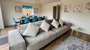 A living room with a sofa, chairs, a dining table, and artwork on the walls. - 4BR Lymington Home near New Forest & Coast (Hampshire)