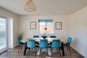 A dining area with a wooden table and teal chairs, a woven pendant light, and two framed artworks on the wall. - Lymington 4BR | New Forest, Coast & Pets (Hampshire)
