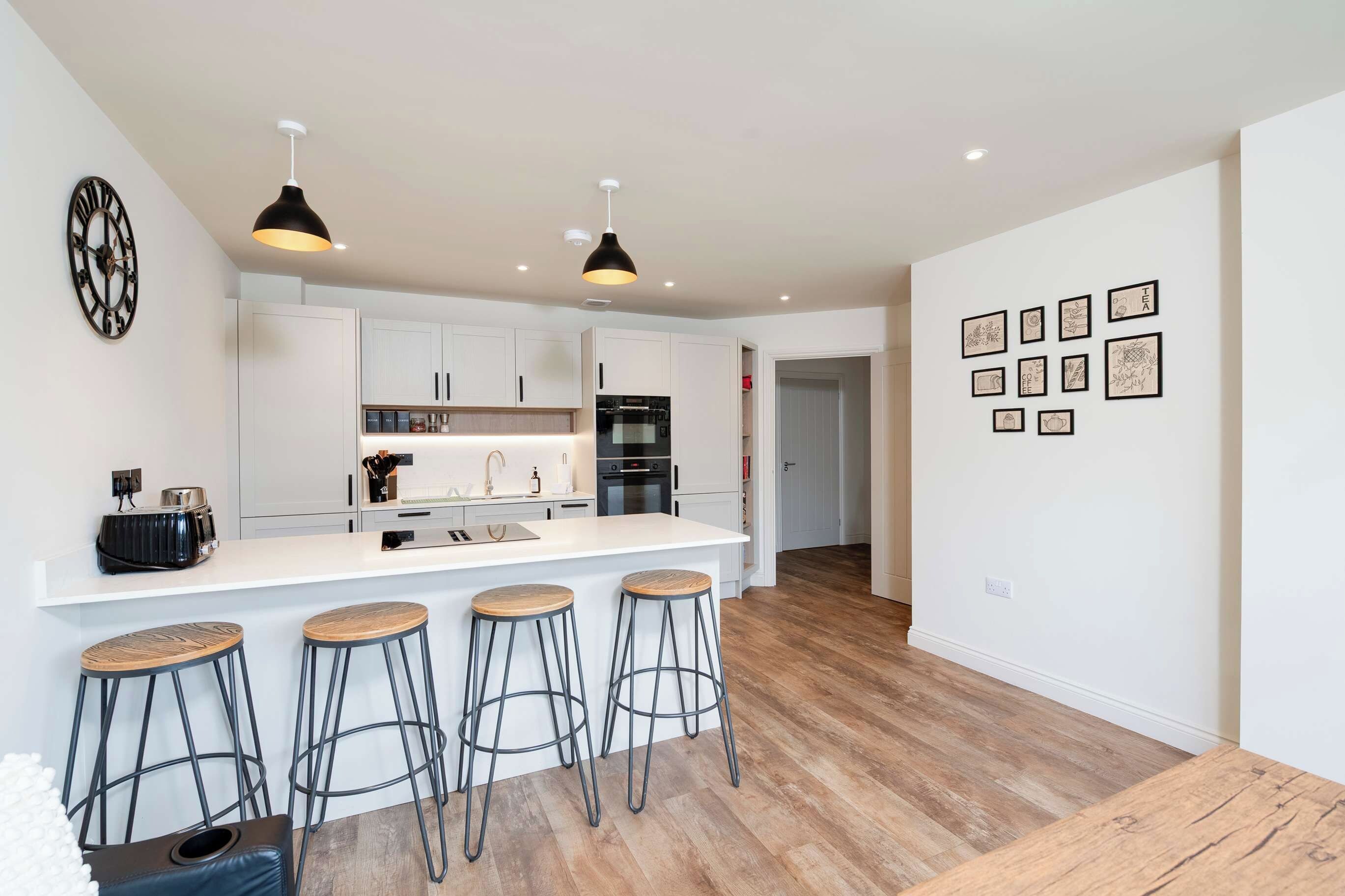 A modern kitchen with white cabinetry, a central island with stools, and a wall with framed pictures.