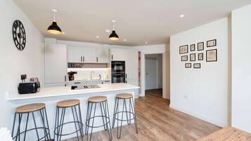 A modern kitchen with white cabinetry, a central island with stools, and a wall with framed pictures.