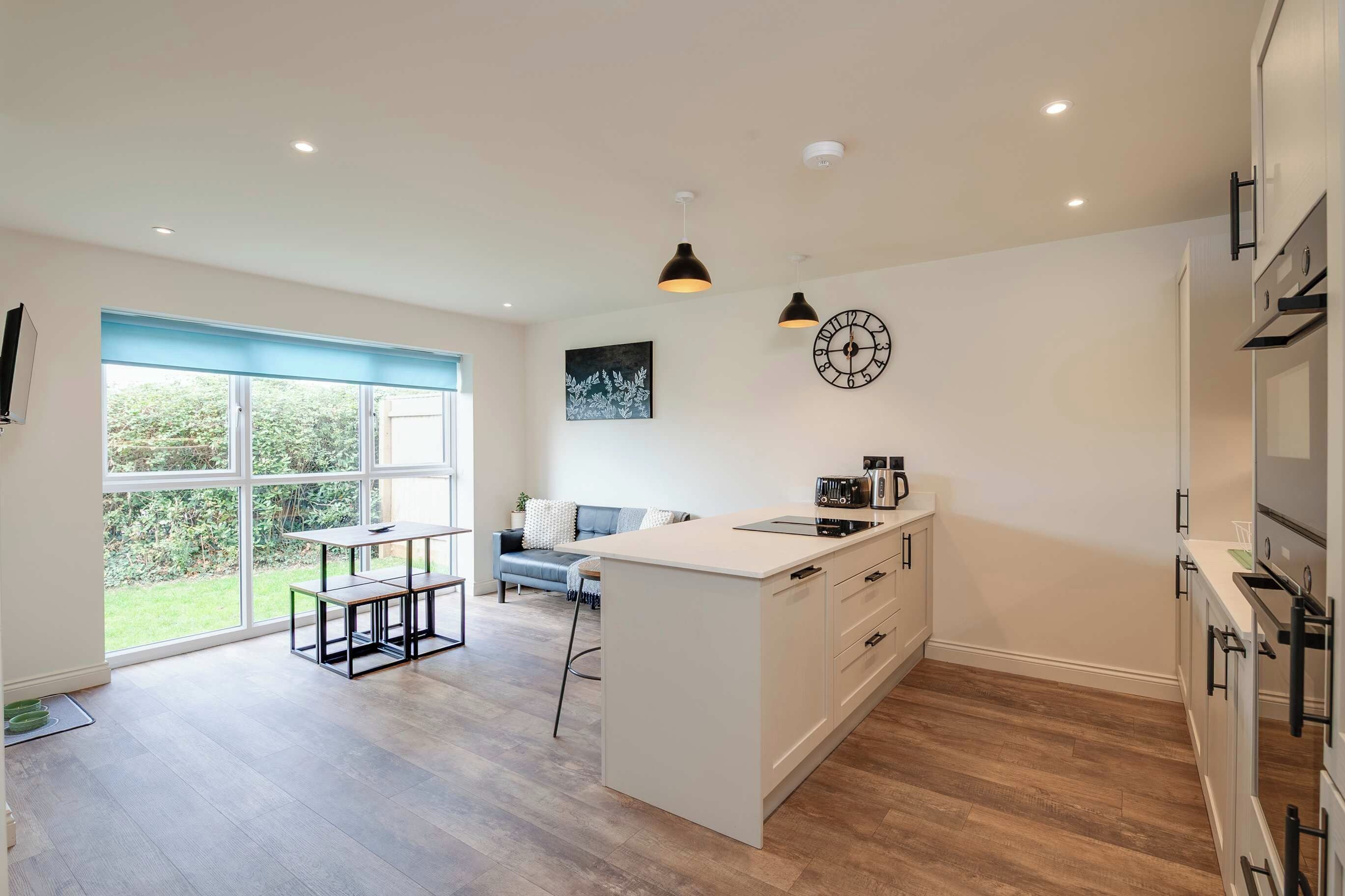 A modern kitchen with a central island, a dining area with a bench, and a large window providing a view of greenery.