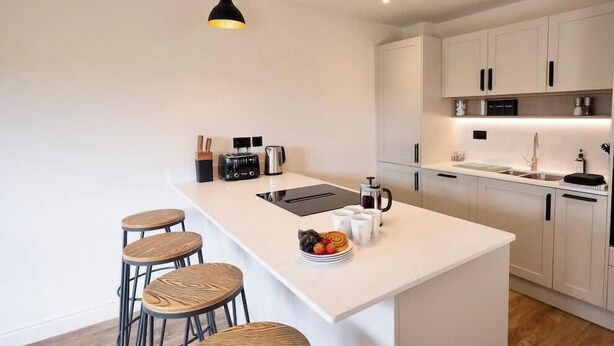 A modern kitchen with a central island, bar stools, a coffee machine, and pendant lighting. - 4BR Lymington Home near New Forest & Coast (Hampshire)