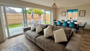 A living room with a sofa, a dining area with chairs, a large sliding glass door leading to a backyard, and a hanging light fixture. - 4BR Lymington Home near New Forest & Coast (Hampshire)