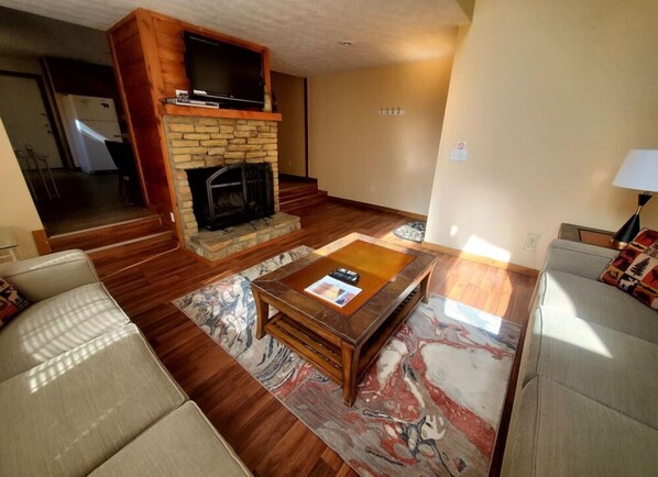 A living room with a fireplace, a television on a wooden shelf, and a coffee table with a magazine.