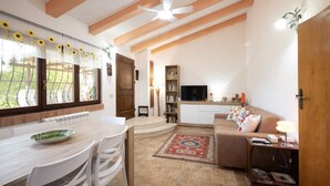 A cozy living room with a sofa, a TV, and a bookshelf. There's a dining area with a table and chairs. - La Casa dei Quadri - Gavorrano (Bivio di Ravi Gavorrano)