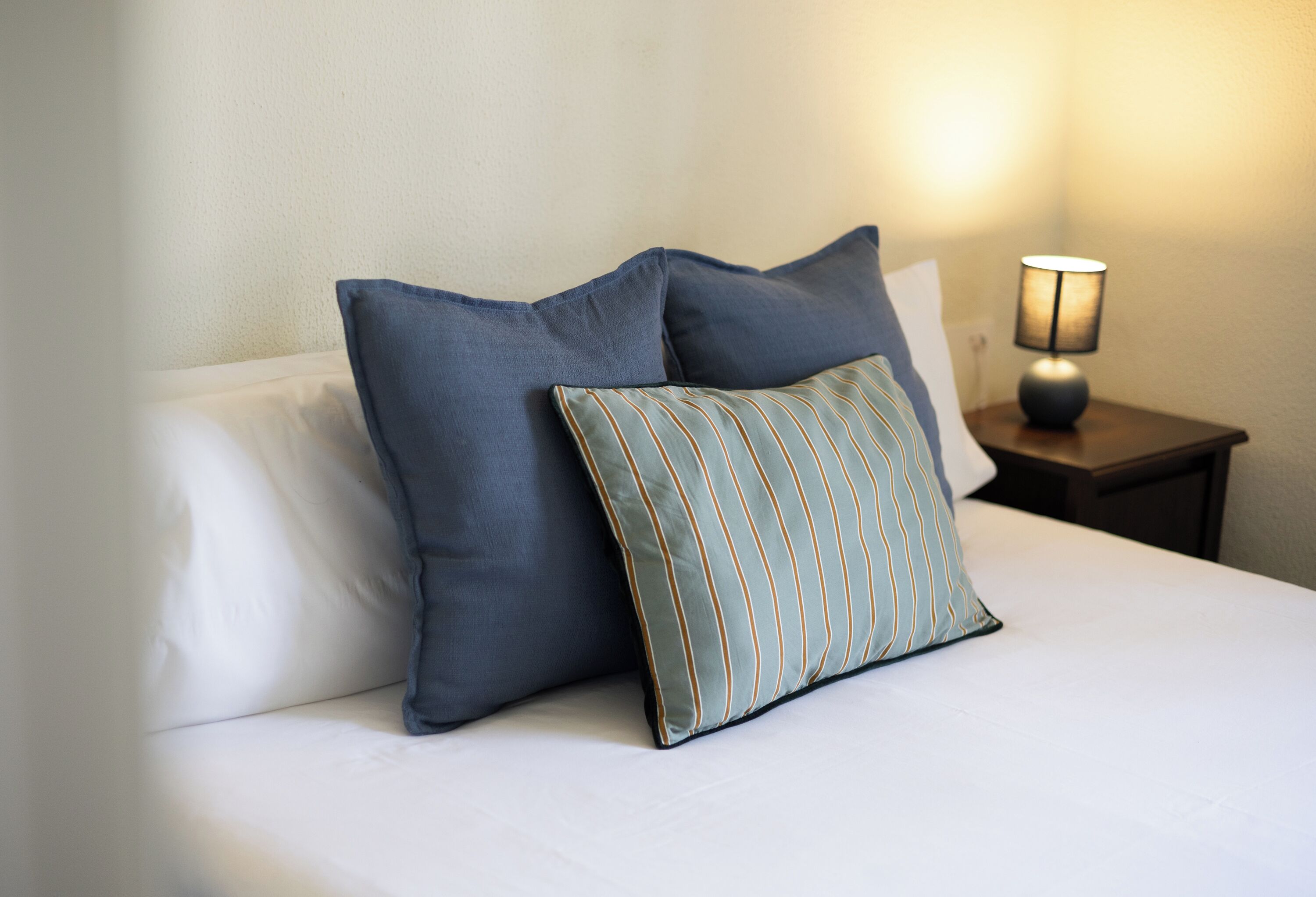A bed with two pillows and a nightstand with a lamp.