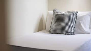 Un lit avec un oreiller à carreaux et un oreiller blanc uni, le tout placé contre un mur uni.